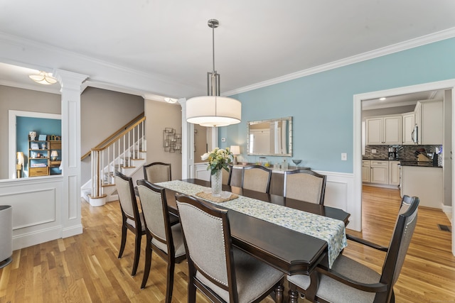 233 Ichabod Rd, Southbury, CT 06488 - dining area featuring ornamental molding, light wood-type flooring, ornate columns, stairway, and wainscoting