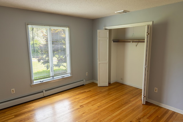 472 Saw Mill Rd, Guilford, CT 06437 - unfurnished bedroom with baseboard heating, light wood-type flooring, multiple windows, a closet, and a textured ceiling