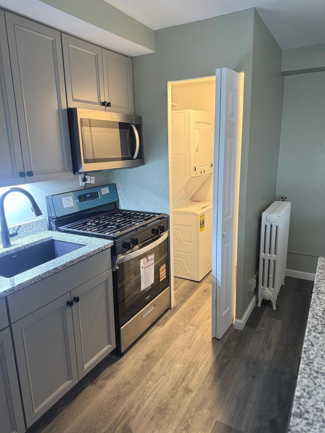 401 Granfield Ave Unit C Bldg 2, Bridgeport, CT 06610 - kitchen featuring appliances with stainless steel finishes, gray cabinetry, stacked washer / dryer, radiator heating unit, and wood finished floors
