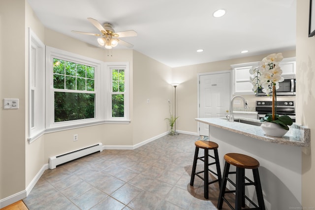 15 Tisbury Rd, Old Lyme, CT 06371 - kitchen featuring a baseboard radiator, appliances with stainless steel finishes, a kitchen breakfast bar, ceiling fan, and light stone countertops