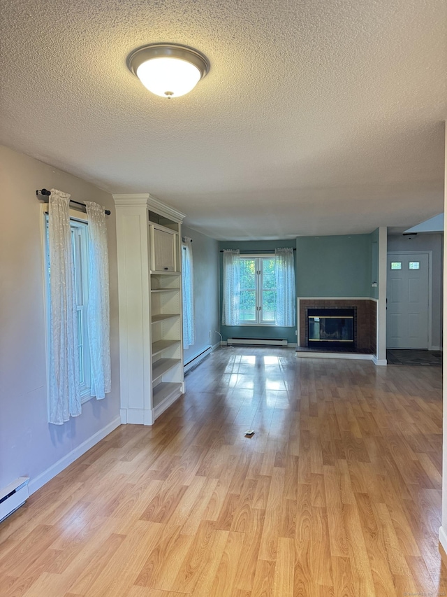 4 Starrwood Dr Unit 4, Norwich, CT 06360 - unfurnished living room with a textured ceiling, a baseboard heating unit, light wood finished floors, and a glass covered fireplace