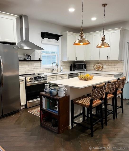 85 W Thames St, Norwich, CT 06360 - kitchen featuring stainless steel appliances, wall chimney range hood, light countertops, a kitchen island, and white cabinets
