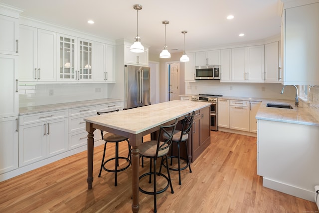 59 Judith Dr, Danbury, CT 06811 - kitchen featuring appliances with stainless steel finishes, white cabinetry, a kitchen island, light wood-type flooring, and backsplash
