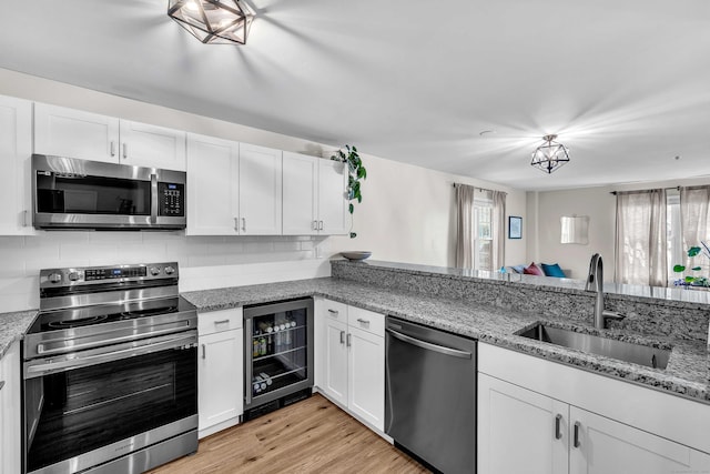 49 Rose St Apt 109, Branford, CT 06405 - kitchen with appliances with stainless steel finishes, beverage cooler, white cabinets, backsplash, and light stone counters