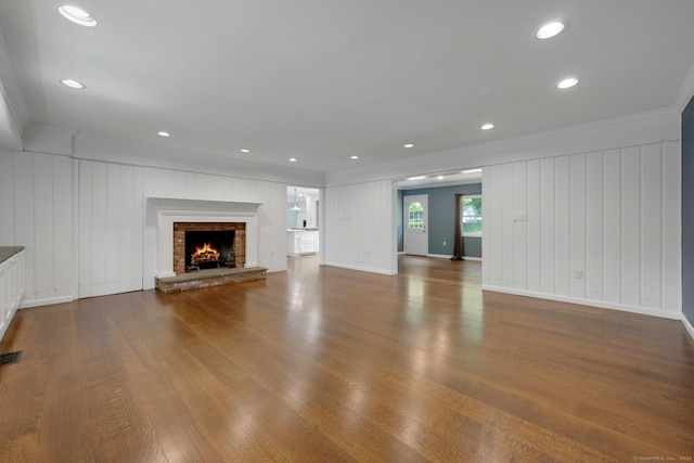46 Bowman Dr, Greenwich, CT 06831 - unfurnished living room featuring ornamental molding, a decorative wall, a brick fireplace, wood finished floors, and recessed lighting