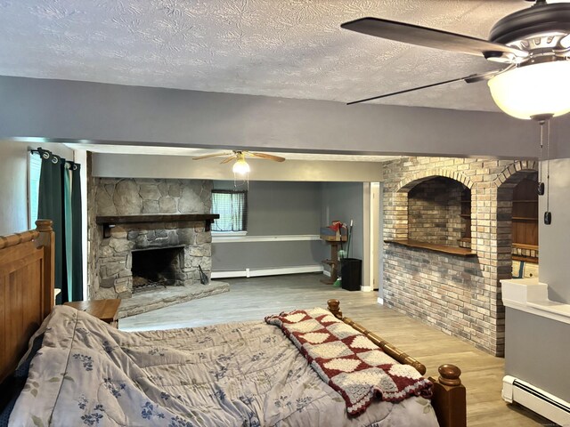 3 Millstream Rd, Hebron, CT 06231 - bedroom with baseboard heating, a stone fireplace, wood finished floors, a textured ceiling, and ceiling fan