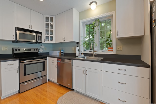 11 Adam Dr, Newington, CT 06111 - kitchen featuring stainless steel appliances, dark countertops, white cabinetry, glass insert cabinets, and light wood-type flooring