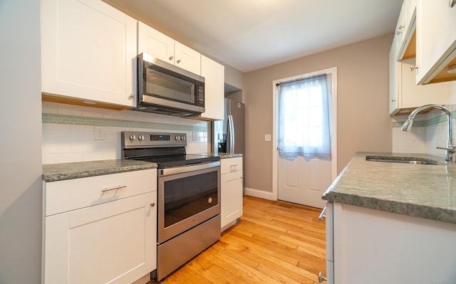 635 Ruth St, Bridgeport, CT 06606 - kitchen with appliances with stainless steel finishes, light wood-style flooring, backsplash, and white cabinets