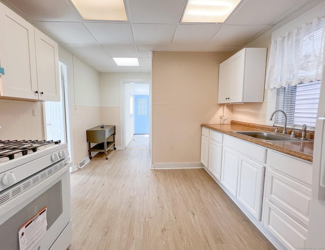 12 Arlington St, West Haven, CT 06516 - kitchen featuring white range with gas cooktop, a paneled ceiling, light wood-style flooring, white cabinets, and healthy amount of natural light