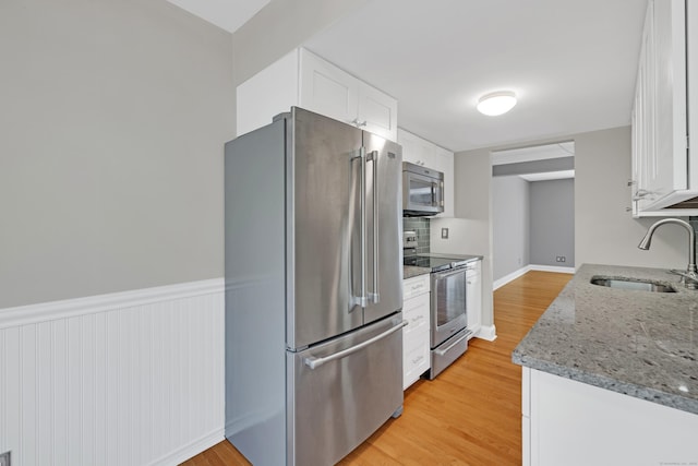97 Park Ave Unit 70, Danbury, CT 06810 - kitchen featuring appliances with stainless steel finishes, white cabinets, light wood-style floors, light stone countertops, and wainscoting