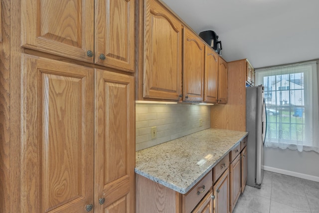 52 Lincoln St, Cromwell, CT 06416 - kitchen featuring freestanding refrigerator, decorative backsplash, light tile patterned flooring, light stone countertops, and brown cabinets