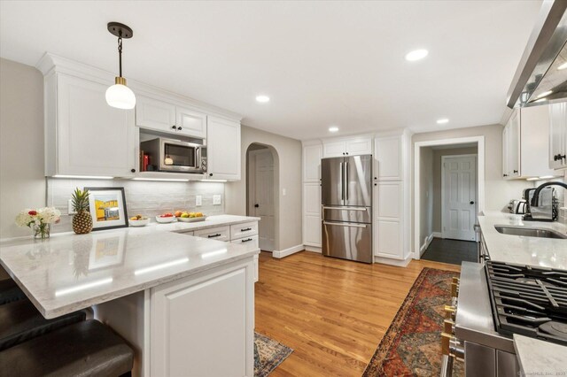 10 Craigmoor Rd, West Hartford, CT 06107 - kitchen featuring appliances with stainless steel finishes, arched walkways, exhaust hood, a peninsula, and light wood finished floors