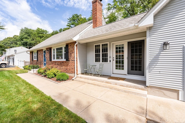 view of exterior entry featuring brick siding, a shingled roof, a chimney, and a yard