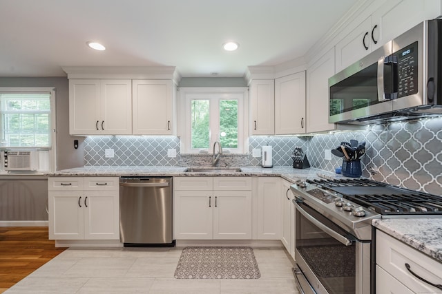 kitchen with stainless steel appliances, white cabinets, plenty of natural light, light stone countertops, and recessed lighting