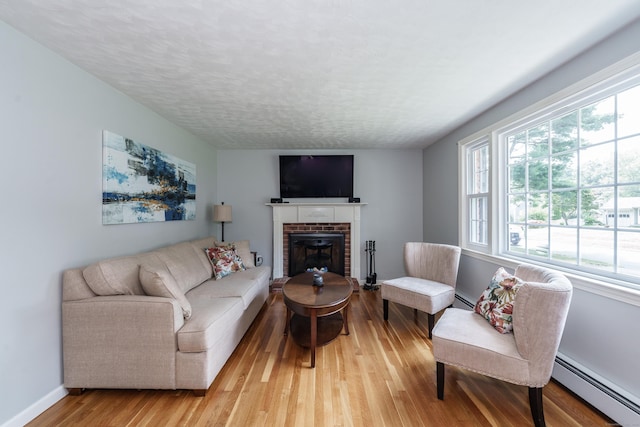 living room with a baseboard heating unit, healthy amount of natural light, a fireplace, light wood-type flooring, and a textured ceiling