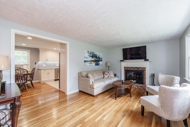 living room with light wood-style floors, a brick fireplace, a textured ceiling, and recessed lighting