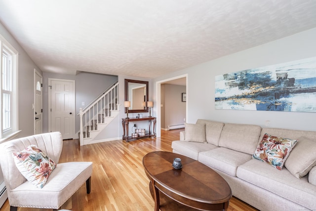 living area featuring baseboard heating, stairs, light wood-type flooring, and a textured ceiling