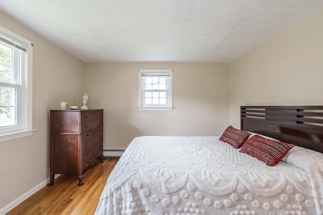 bedroom with baseboard heating and wood finished floors