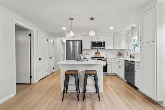103 Perry Rd, Bristol, CT 06010 - kitchen with appliances with stainless steel finishes, white cabinetry, light wood-style floors, a kitchen breakfast bar, and decorative backsplash