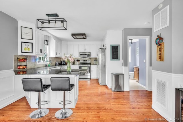 51 Olde Village Cir Unit 51, Wallingford, CT 06492 - kitchen with stainless steel appliances, a peninsula, backsplash, white cabinets, and light wood finished floors