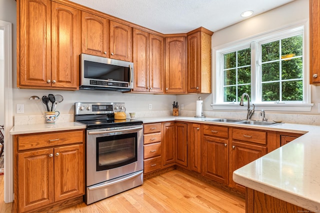 132 Deerwood Rd, Tolland, CT 06084 - kitchen featuring appliances with stainless steel finishes, light wood-type flooring, brown cabinetry, and a textured ceiling
