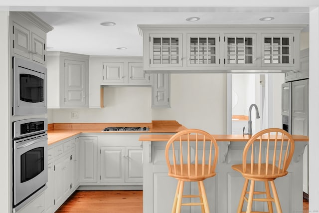 795 Rte 148, Killingworth, CT 06419 - kitchen featuring appliances with stainless steel finishes, a breakfast bar, light countertops, glass insert cabinets, and light wood-style flooring