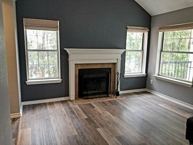 31 High St Apt 11206, East Hartford, CT 06118 - unfurnished living room with vaulted ceiling, healthy amount of natural light, a tiled fireplace, wood finished floors, and a textured wall
