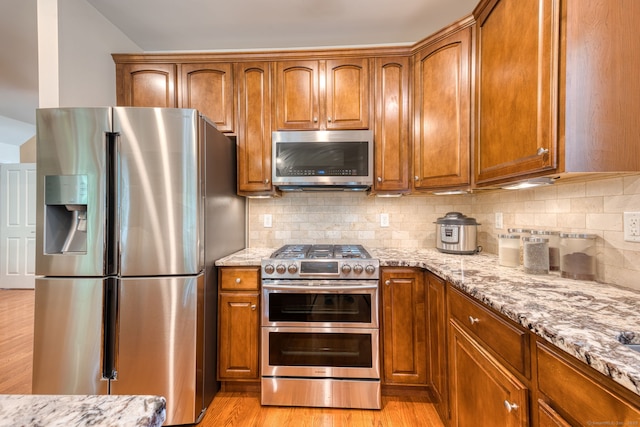 188 Sterling Dr Unit 188, Newington, CT 06111 - kitchen with appliances with stainless steel finishes, light stone counters, brown cabinetry, light wood-style floors, and tasteful backsplash