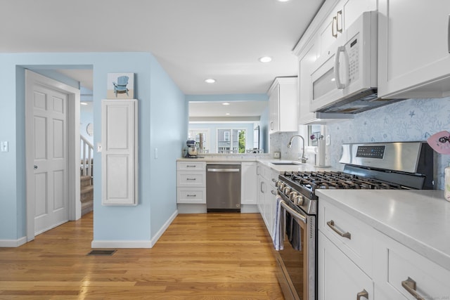 35 Lawrence Ave, Milford, CT 06460 - kitchen with appliances with stainless steel finishes, light wood-style flooring, white cabinets, tasteful backsplash, and light countertops