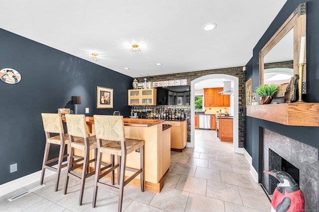 10 Prynne Ridge Rd, Longmeadow, MA 01106 - kitchen with a kitchen bar, a fireplace, arched walkways, wall chimney range hood, and glass insert cabinets