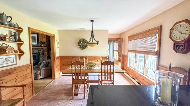 70 River Rd, Preston, CT 06365 - dining area with wainscoting, tile patterned floors, a baseboard radiator, a stone fireplace, and wooden walls