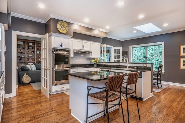 6 Salisbury Way, Farmington, CT 06032 - kitchen with stainless steel double oven, a skylight, white cabinetry, ornamental molding, and a kitchen bar