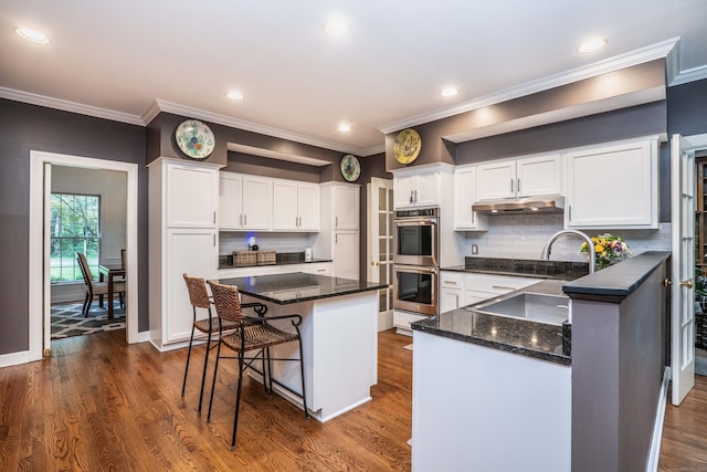 6 Salisbury Way, Farmington, CT 06032 - kitchen with stainless steel double oven, white cabinets, under cabinet range hood, a breakfast bar area, and ornamental molding
