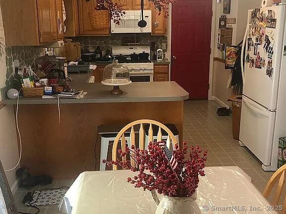 26 Julia Ln, Thomaston, CT 06787 - kitchen featuring white appliances, brown cabinets, a peninsula, light tile patterned floors, and backsplash