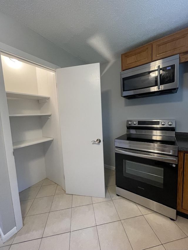 56 Elm St Apt 36, Enfield, CT 06082 - kitchen with stainless steel appliances, light tile patterned floors, a textured ceiling, brown cabinets, and dark countertops