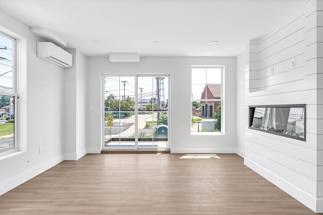 32 Broadway Ave, Stonington, CT 06355 - unfurnished living room featuring a wall mounted air conditioner, light wood-style floors, and a glass covered fireplace