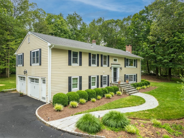 58 Longmeadows Rd, Wilton, CT 06897 - split foyer home with a chimney, an attached garage, a front lawn, asphalt driveway, and view of wooded area
