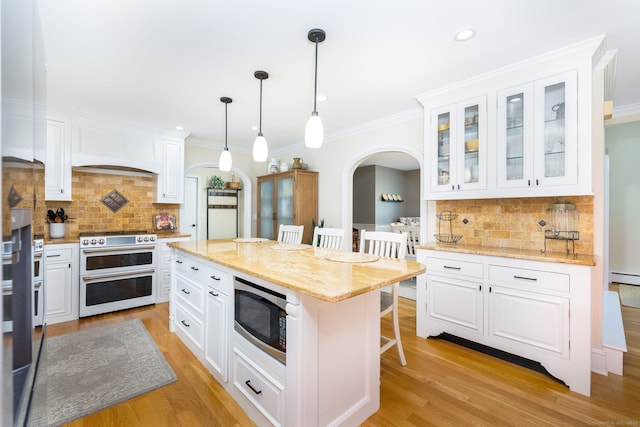 89 Honey Hill Rd, New Hartford, CT 06057 - kitchen featuring range with two ovens, stainless steel microwave, a breakfast bar, arched walkways, and white cabinets