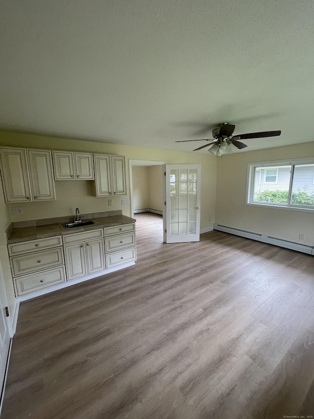 37 W Normandy Dr, West Hartford, CT 06107 - unfurnished living room with light wood-style flooring, baseboard heating, ceiling fan, and a textured ceiling