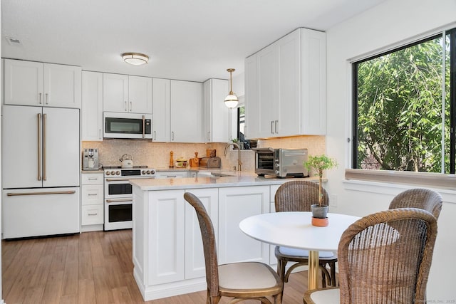 583 Heritage Vlg Unit A, Southbury, CT 06488 - kitchen with premium appliances, light countertops, a peninsula, decorative backsplash, and white cabinetry