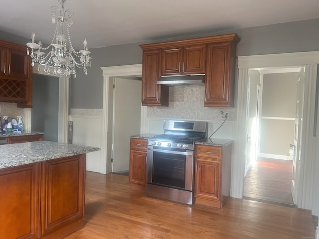 155 Summerfield Ave, Bridgeport, CT 06610 - kitchen featuring stainless steel gas stove, under cabinet range hood, light stone counters, and a chandelier
