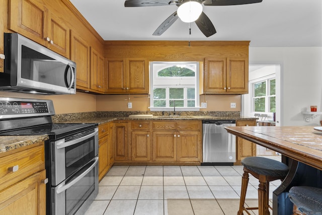 124 Pulaski Hwy, Ansonia, CT 06401 - kitchen with appliances with stainless steel finishes, brown cabinetry, light tile patterned floors, ceiling fan, and dark stone countertops