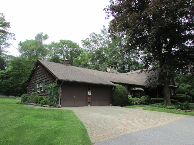 view of front of home featuring decorative driveway, an attached garage, a chimney, a front lawn, and a shingled roof