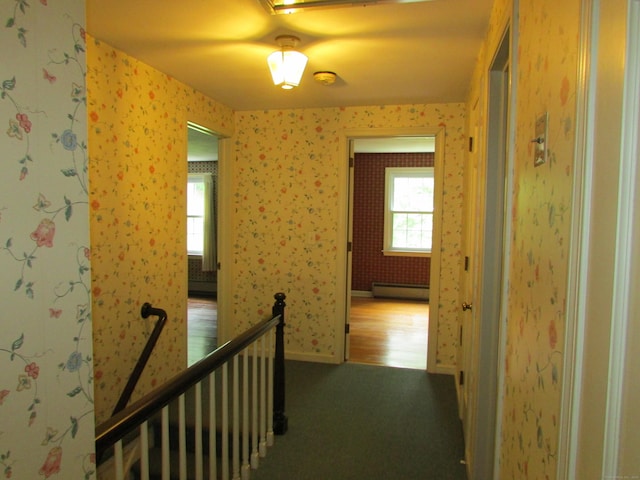 corridor featuring baseboard heating, carpet, an upstairs landing, and wallpapered walls