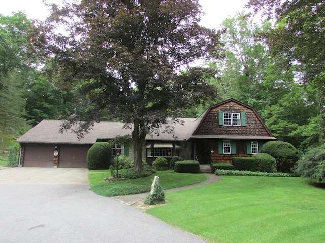 view of front facade with driveway, a gambrel roof, an attached garage, a front yard, and a shingled roof