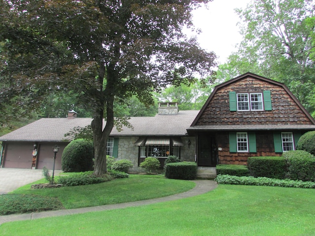 view of front facade featuring a chimney, an attached garage, driveway, a front yard, and a gambrel roof