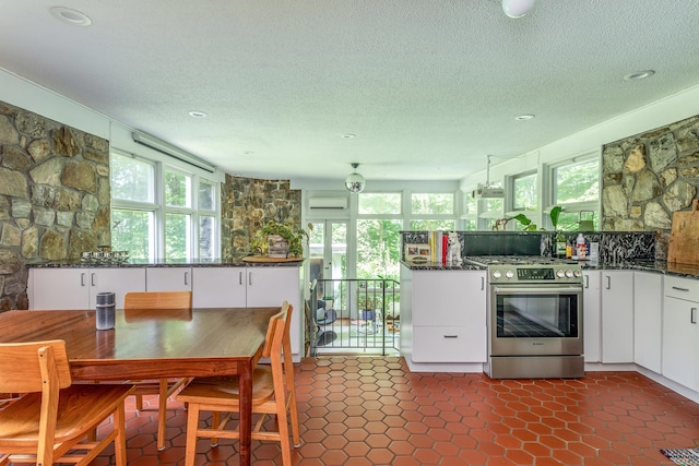 96 Sherman Rd, New Milford, CT 06776 - kitchen with stainless steel gas range oven, white cabinetry, a textured ceiling, a wall unit AC, and dark stone countertops