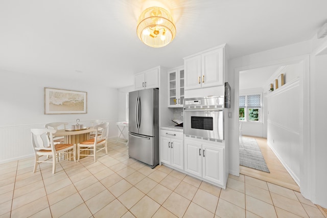 33 Ridgeley St, Darien, CT 06820 - kitchen with appliances with stainless steel finishes, light tile patterned floors, a chandelier, white cabinetry, and glass insert cabinets