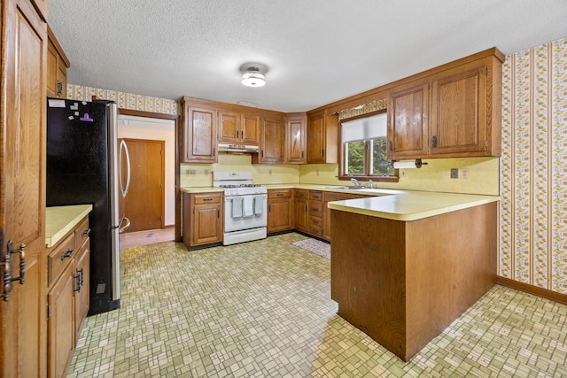 229 Flanders Rd, Southington, CT 06489 - kitchen with white gas range, wallpapered walls, freestanding refrigerator, a peninsula, and brown cabinetry