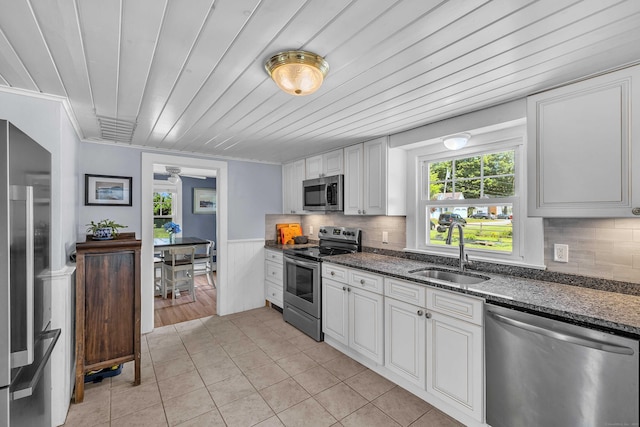 18 Lynde St, Old Saybrook, CT 06475 - kitchen with stainless steel appliances, dark stone countertops, a wainscoted wall, light tile patterned flooring, and white cabinets